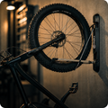 alt="Support vélo mural rabattable Sykell noir installé dans un garage à Six-Fours-les-Plages, Var, maintenant un VTT électrique par la roue."